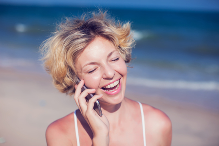 Young happy woman talking on mobile phone on a beach with sea backgroundの写真素材