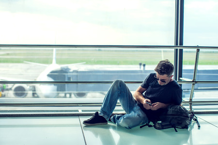 Young man checking his phone while waiting his flight in the airport. Travel conceptの写真素材