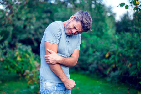 People, healthcare and problem concept - unhappy man with dark hair suffering from elbow pain outdoorの写真素材
