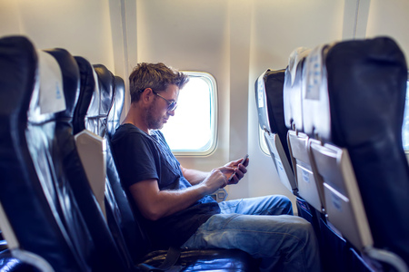 Man with dark hair is reading text message on mobile phone and speaking by phone during flying in the airplaneの写真素材
