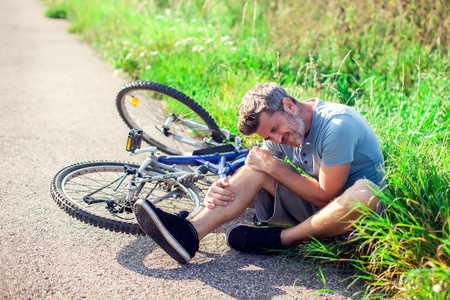 Man with dark hair with pain in knee joints after biking on bicycle. Sport, healthcare and people conceptの写真素材