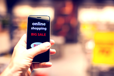 People, sale, consumerism, advertisement and black friday concept - close up of man's hand holding shopping bags and smartphone with shopping online inscription at the mallの写真素材