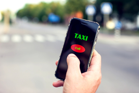 Male hand with smartphone on blurred road background. Taxi service application on the screen.の写真素材