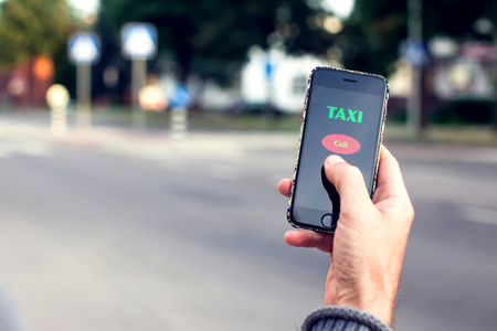 Male hand with smartphone on blurred road background. Taxi service application on the screen.の写真素材