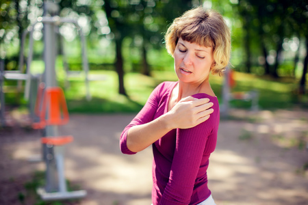 Young woman feeling pain in her shoulder during sport workout in the park. Sport, medicine and people conceptの写真素材