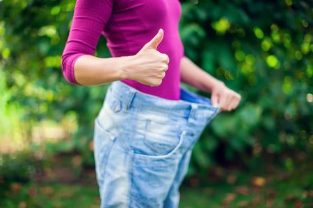 Young woman wearing big loose jeans with apple in hand outdoor- weight loss conceptの写真素材