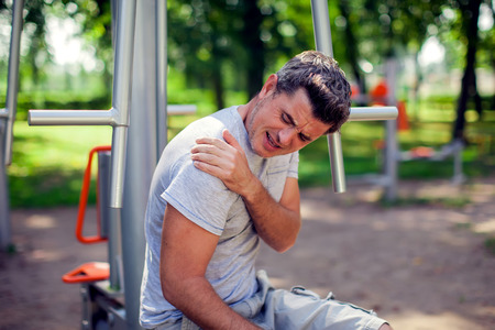 Au unhappy man feeling pain in his shoulder during sport and workout in the park. Sport, medicine and people conceptの写真素材