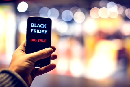 People, sale, consumerism, advertisement concept - close up of man's hand holding shopping bags and smartphone with black friday inscription at the mallの写真素材