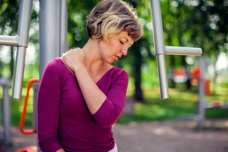 Young unhappy woman feeling pain in her neck during sport workout in the park. Sport, medicine and people conceptの写真素材
