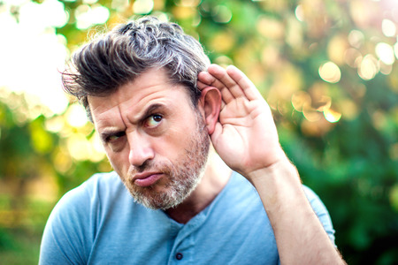 Listening.Close up on hand man and ear listening for a quiet sound or paying attention outdoorの写真素材