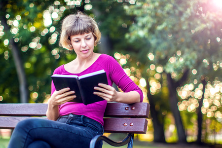 A blonde woman sitting and reading a book outdoor. People, lifestyle conceptの写真素材