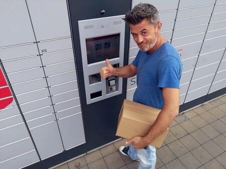 Man client using automated self service post terminal machine or locker to deposit a parcel for storageの写真素材
