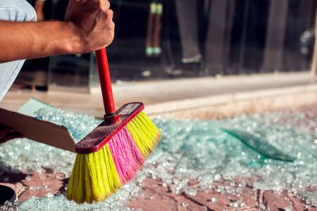 Man sweeps a lot of small shards of glass away on the ground outdoor
