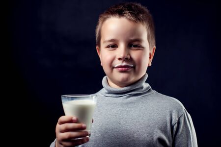 A portrait of a boy with glass of milk in front of dark background. Children, drink and food conceptの写真素材