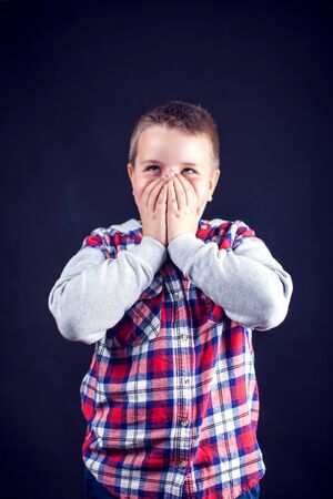 A boy closed his mouth with hands. Children and emotions conceptの写真素材