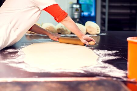 A chef rolls out the doughon on black table.の写真素材