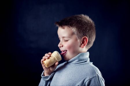 A portrait of a cute boy with icecream in front of dark background. Children and food conceptの写真素材