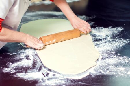 A chef rolls out the doughon on black table.