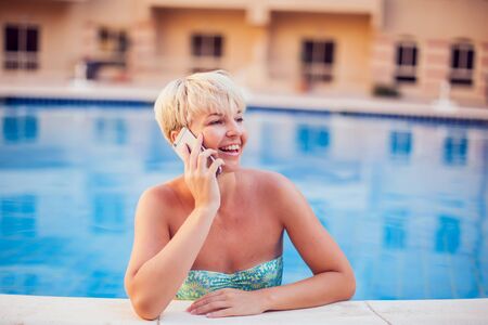 Woman spends time and has relax on the pool with phone. People, summer, holiday and technology conceptの写真素材