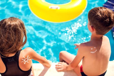 Children with sun protection cream on skin have fun in the pool. Children, summer, holiday and...