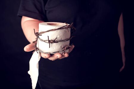 Woman holds toilet paper with barbed wire around it on black background. People, healthcare and medicine concept.の写真素材