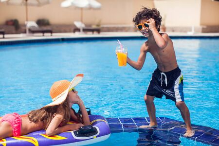 Two happy kids girl and boy drink juice in the pool and have fun. Children and summer concept