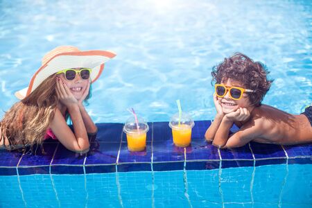 Two happy kids girl and boy drink juice in the pool and have fun. Children and summer conceptの写真素材