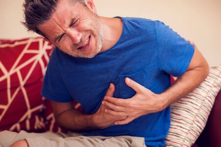 Man feels strong heart pain at home. People, healthcare and medicine concept