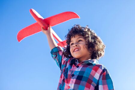 Young happy boy playing with red airplane outdoor. Children and entertainment concept