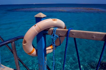 Red emergency lifebuoy hanging on fence near sea or poolの写真素材