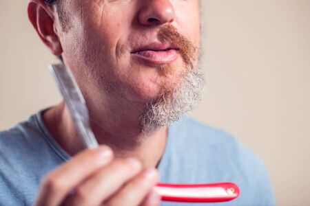 A portrait of man with half beard and hair holds razor in his hand