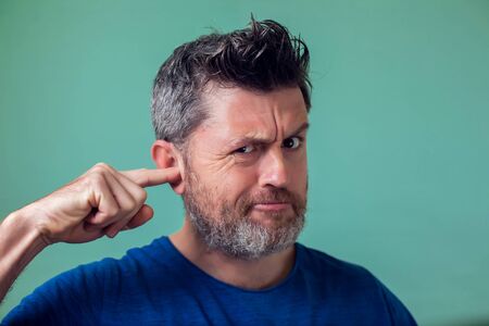 Young man with beard picking his ear with his finger- people, healthcare and emotionsの写真素材
