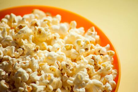 An orange bowl with popcorn isolated on yellow background. Food conceptの写真素材