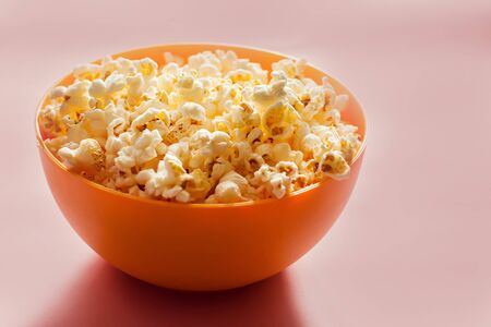 An orange bowl with popcorn isolated on pink background. Food conceptの写真素材