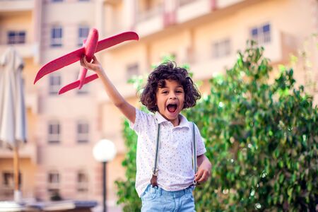 Young happy boy playing with red airplane outdoor. Children and entertainment concept