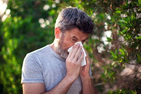 Man blowing nose in front of blooming tree. Spring allergy and healthcare conceptの写真素材