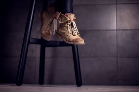 Dark low section of woman wearing boots sitting at bar counter in cafe