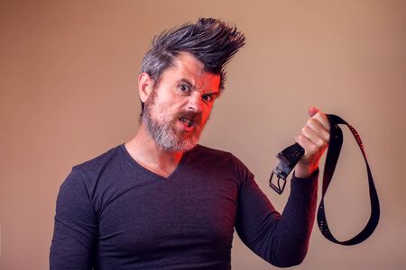 Angry bearded man holds belt in hand. Emotions and family violence concept