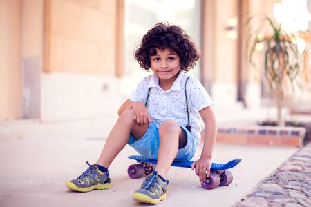 Little boy with curly hair with skateboard outdoor. Children and entertainment conceptの写真素材