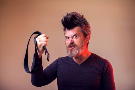 Angry bearded man holds belt in hand. Emotions and family violence concept