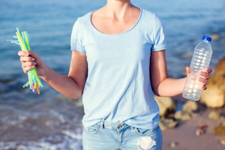 Woman holds plastic bottle and straws in hands on the beach. Plastic Pollution concept.の写真素材
