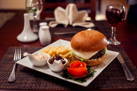Large tasty burger with French fries in a cafe on a white plateの写真素材