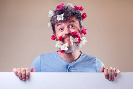 Handsome smiled man with flowers on his beard and hair. People, emotions, summer or spring conceptの写真素材