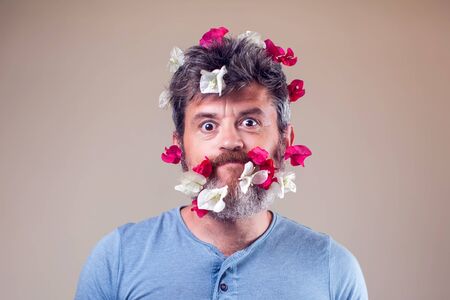 Handsome smiled man with flowers on his beard and hair. People, emotions, summer or spring conceptの写真素材