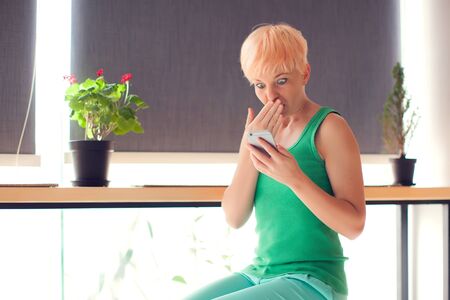 Surprised young woman relaxing at home chatting with her touch screen smartphone. People, emotion and technology conceptの写真素材