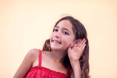 Little girl keeps hand near her ear and smile. Children and emotions concept.の写真素材