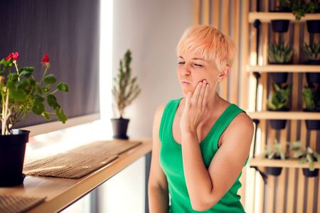A woman with pain in her teeth is holding her face indoor. People, health care and medical conceptの写真素材