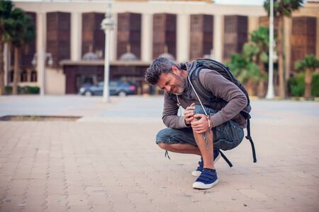 Close up of a man sitting and holding his knee in pain due to injury outdoor. People, health care, medical conceptの写真素材