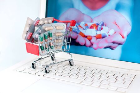 Full small shopping trolley of pills at laptop on white background. Health and medicine concept. Online shopping and medicine conceptの写真素材