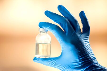 A doctor in blue gloves holding a bottle with vaccine. Close up shot. Medicine and healthcare conceptの写真素材